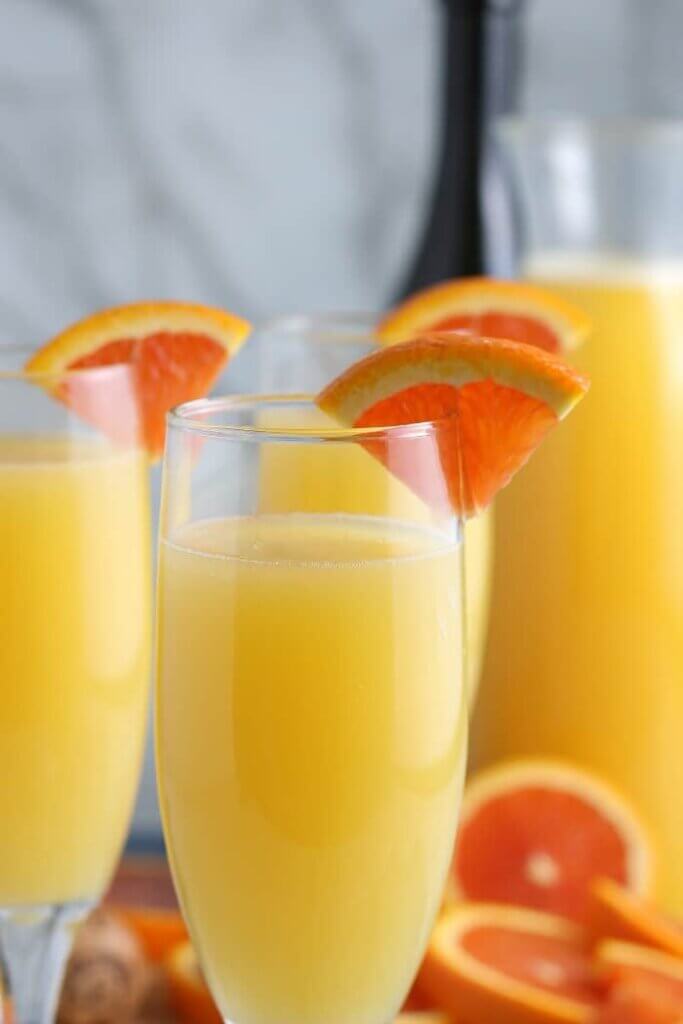 Extreme closeup of glass flutes filled with bright yellow cocktails and a slice or orange on the rim.