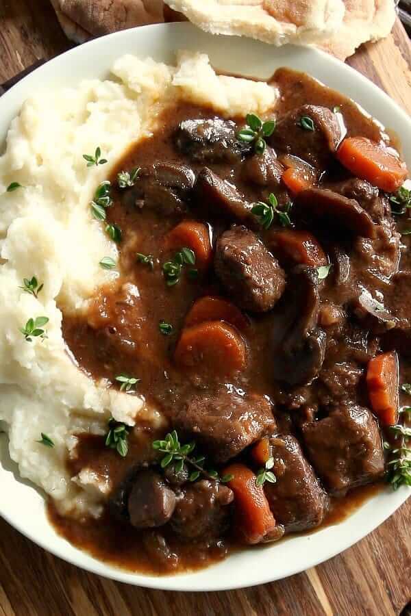 Overhead view of a plateful of rich sauced vegan stew over mashed potatoes. Ripped bread on the side for dipping.