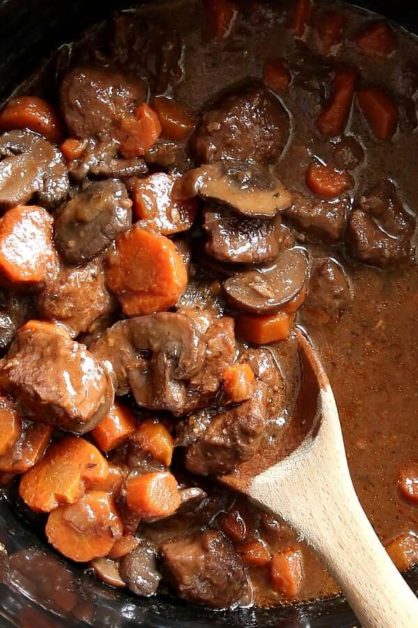 Close up of a wooden spoon dishing out Beef Bourguignon Recipe from the Slow Cooker.