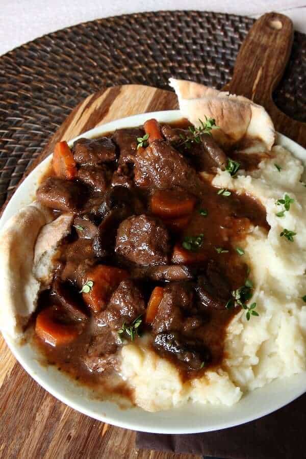 Tilted plate full of mashed potatoes and topped with juicy stew with carrots.