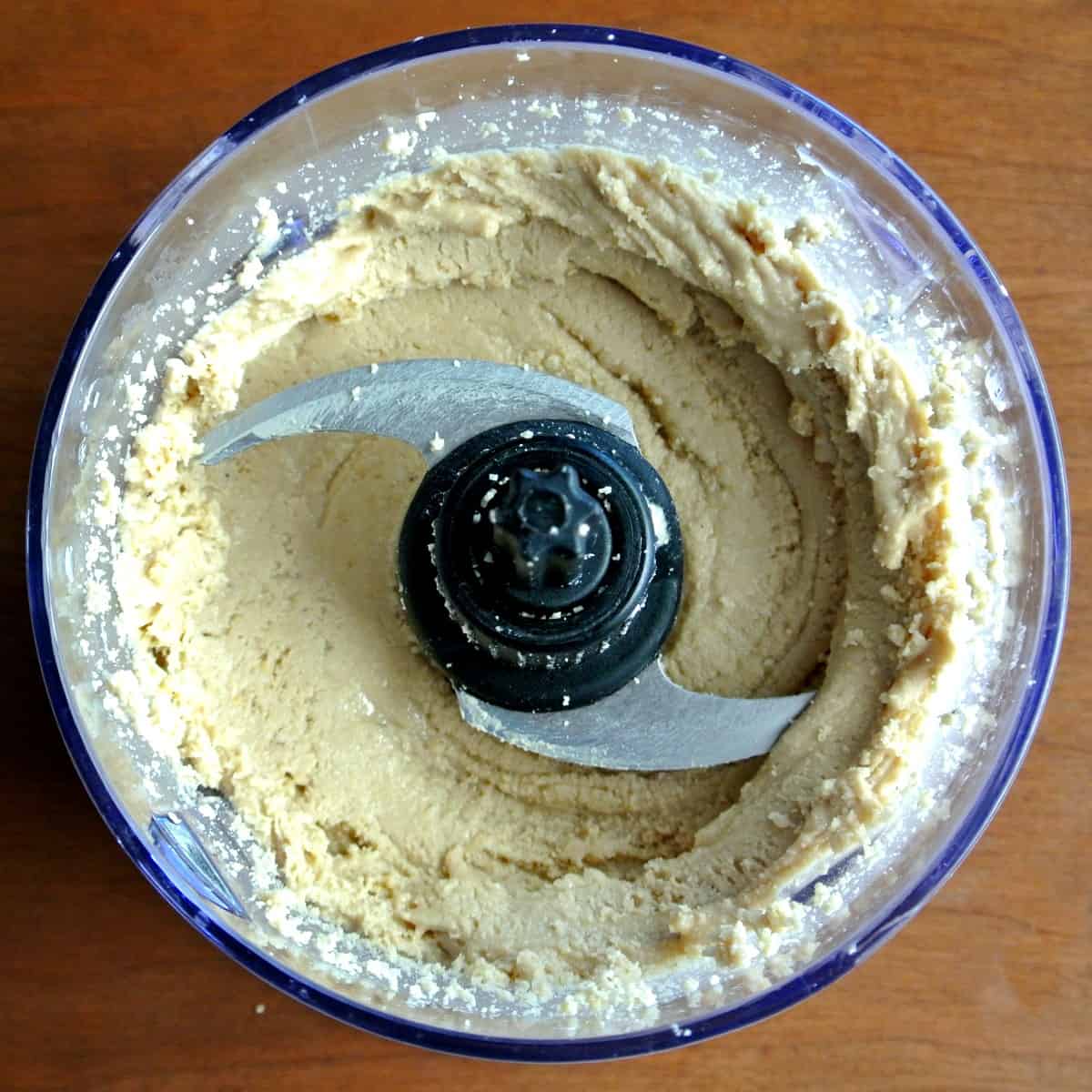 Looking down into a small food processor where cashews have just started to get creamy.