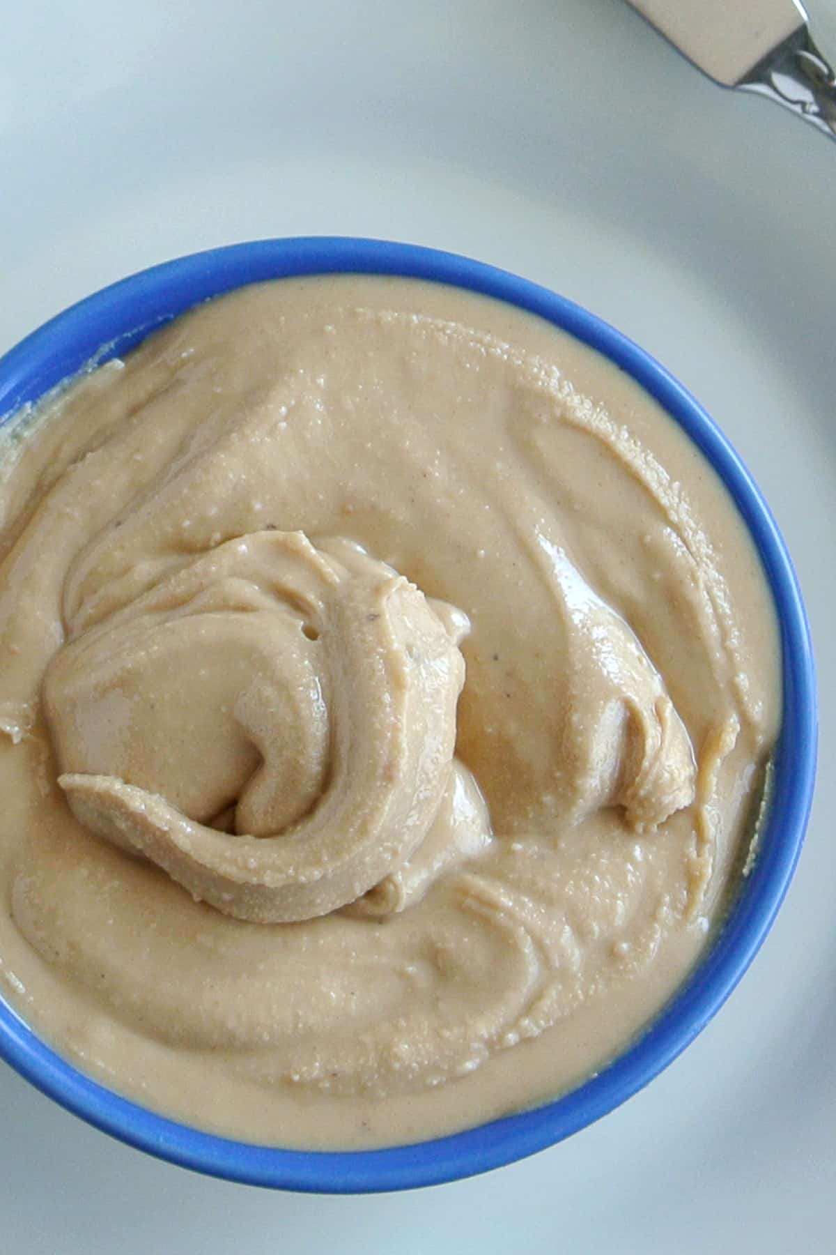 Very close up photo of creamy swirled cashew butter in a blue bowl on a white plate.
