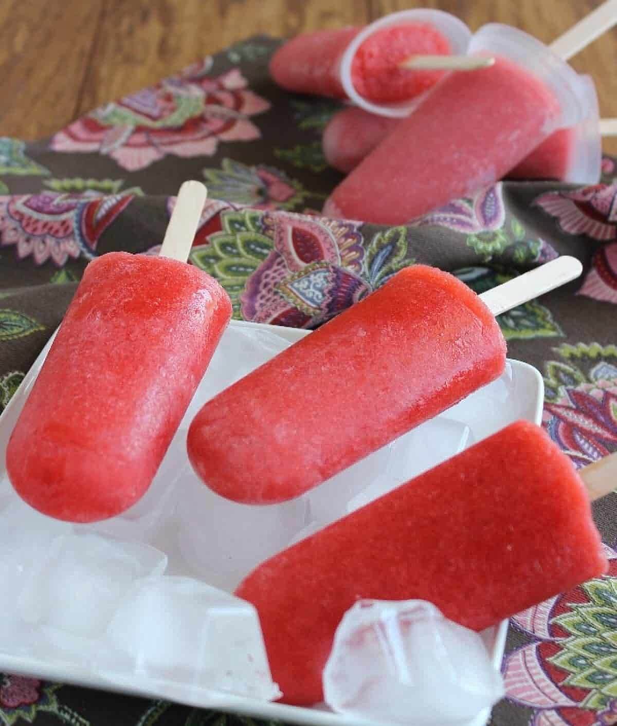 Side angle of six red popsicles. Three are on a bed of ice and three are still in their molds.