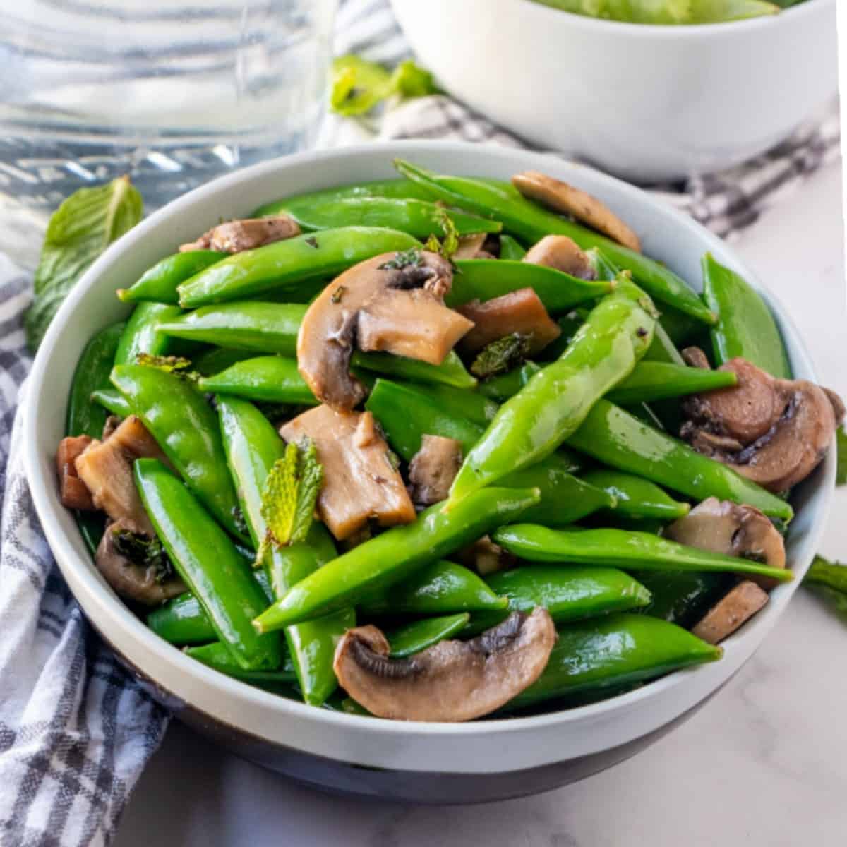 Tilted forward and centered bowl of a green veggie side dish with a plaid handtowel on the side.