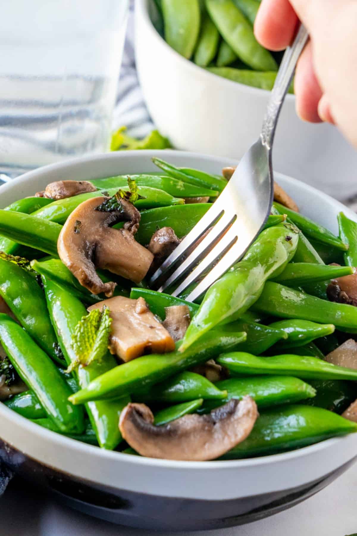 Angled bowl full of sugar snap peas with a fork pulling up the first bite.