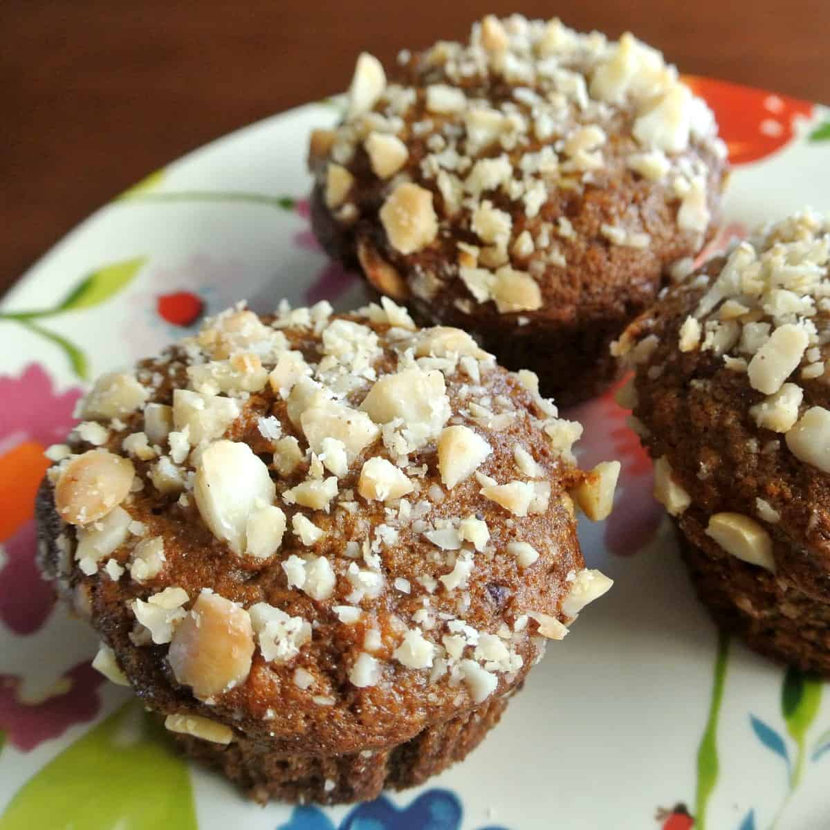 Angled photo of three muffins on a flowered plate with nuts acattered.