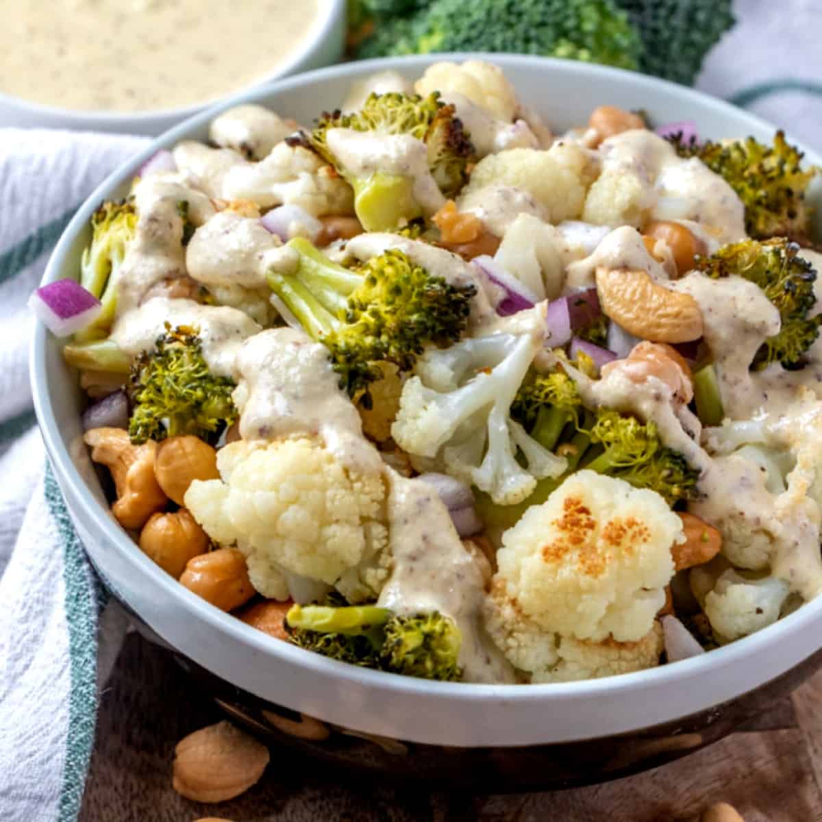 Roasted vegetables tossed in a white bowl and covered with creamy sauce.