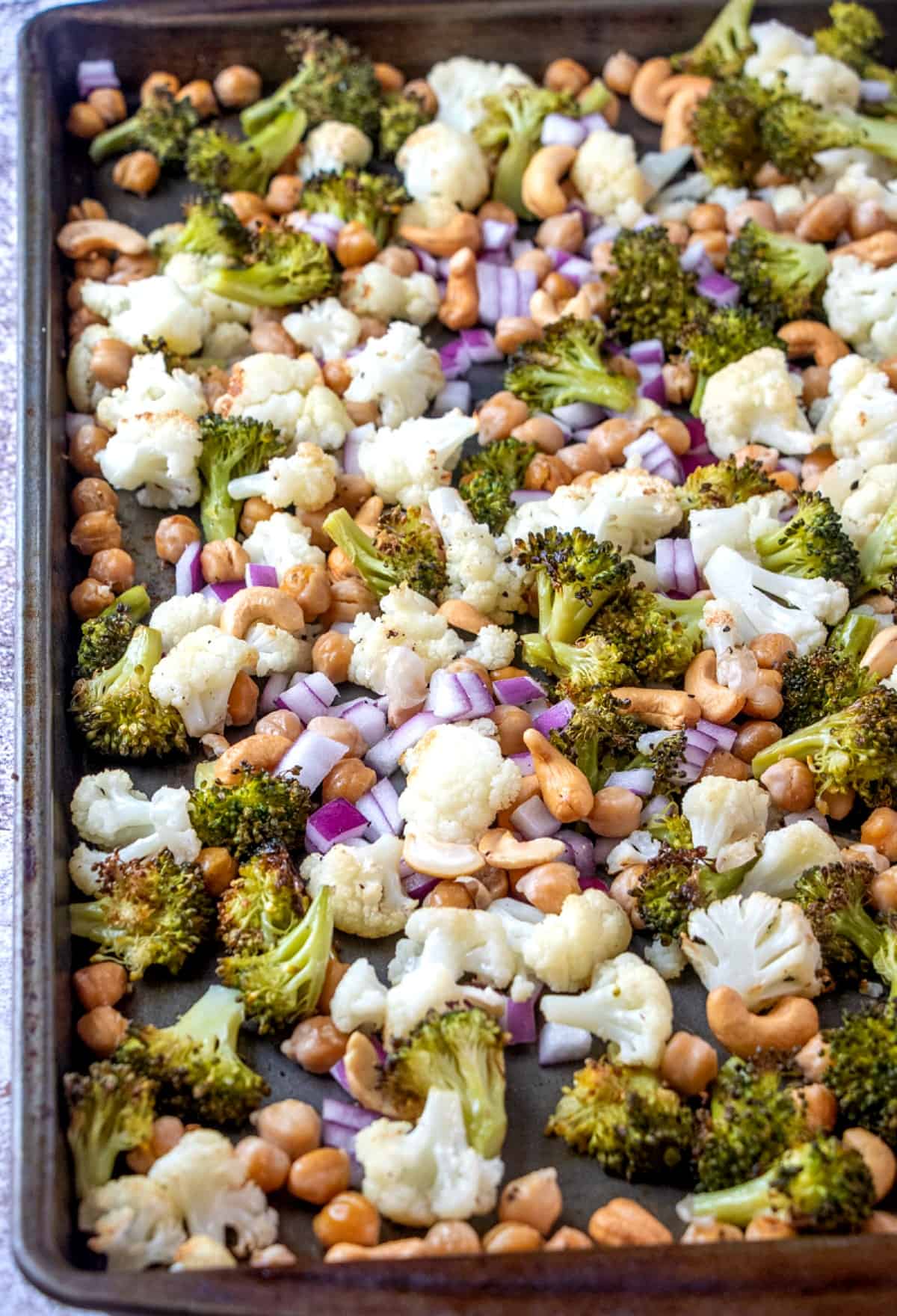 Mixed vegetable bites with cashews are roasted and on a baking sheet.