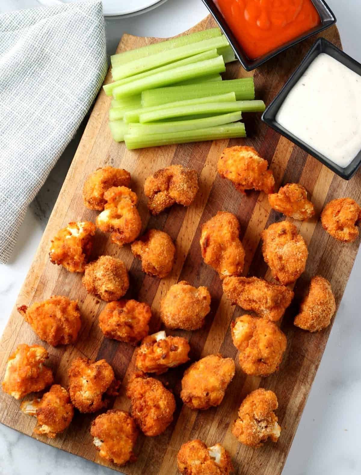 Perfect bite size air fryed cauliflower bites covered in a spicy mix. All are on a wooden cutting board.