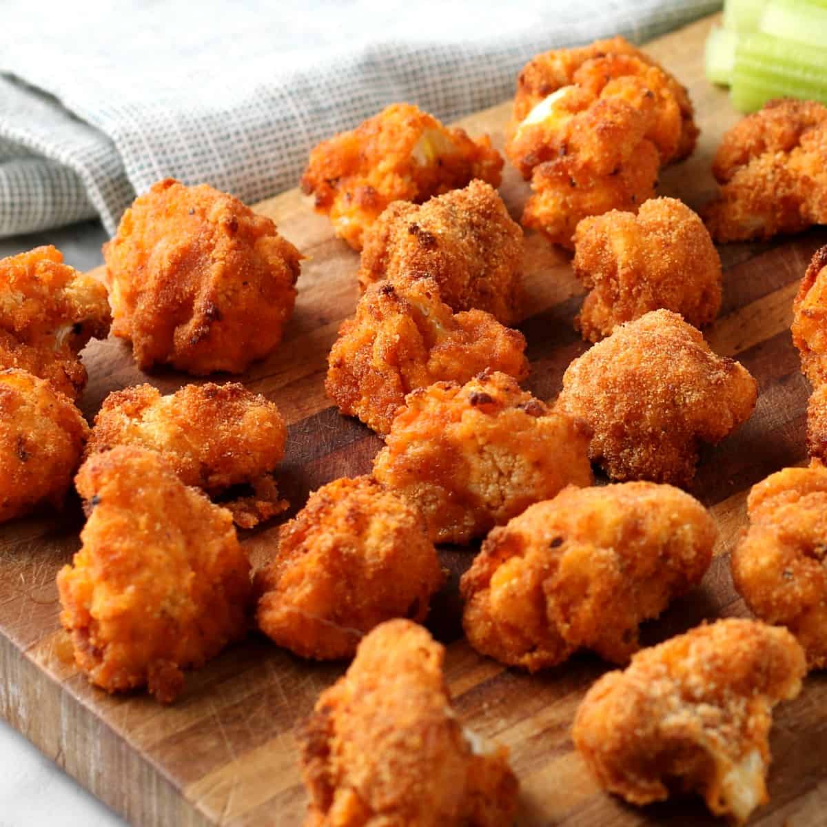 Close up square photo of multiple cauliflower buffalo bites strewn across a wooden cutting board.
