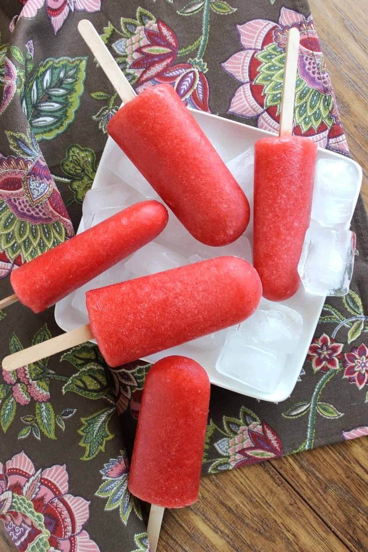 Overhead view of red frozen treats laying on a bed of ice and a square white plate.