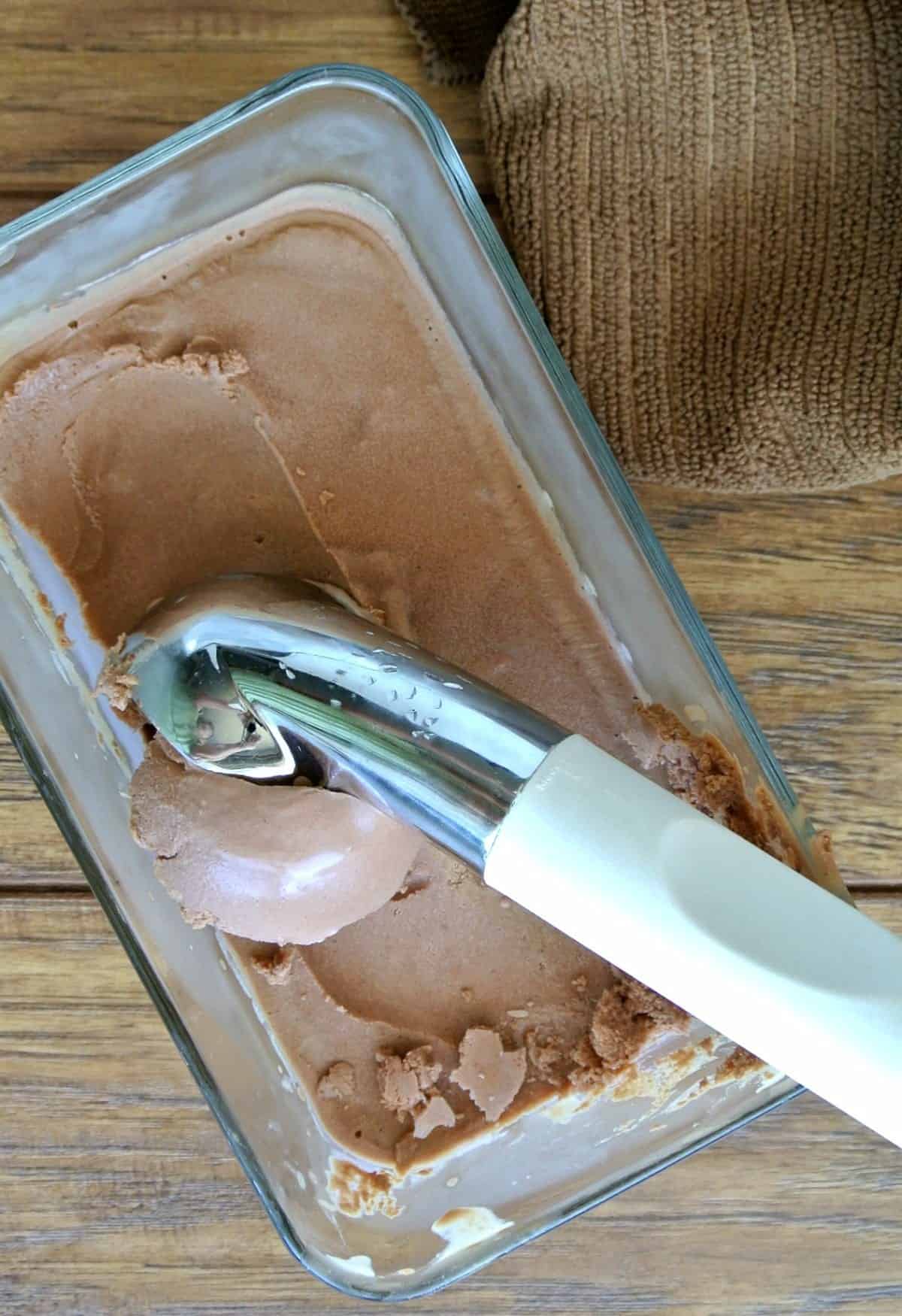 Stainless Steel ice cream scoop is scooping up a big serving of chocolate out of a glass container.