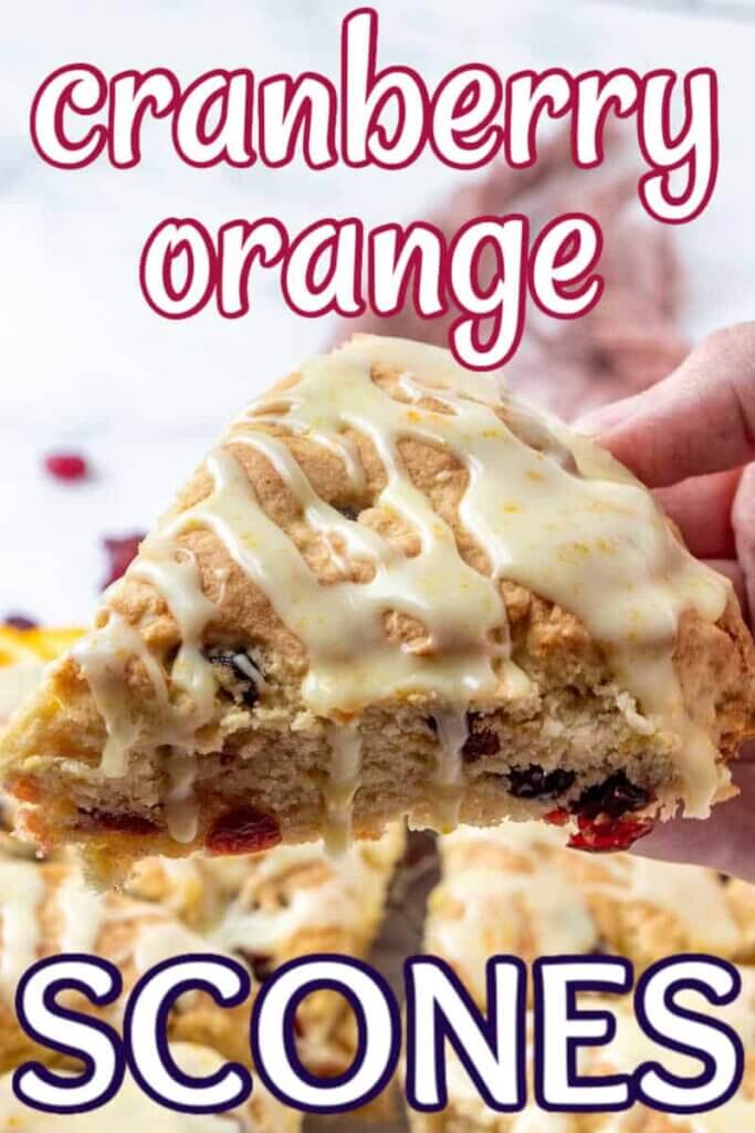A hand is holding a triangle piece of Cranberry Orange Scones close to the camera so you can see the zest in the icing.