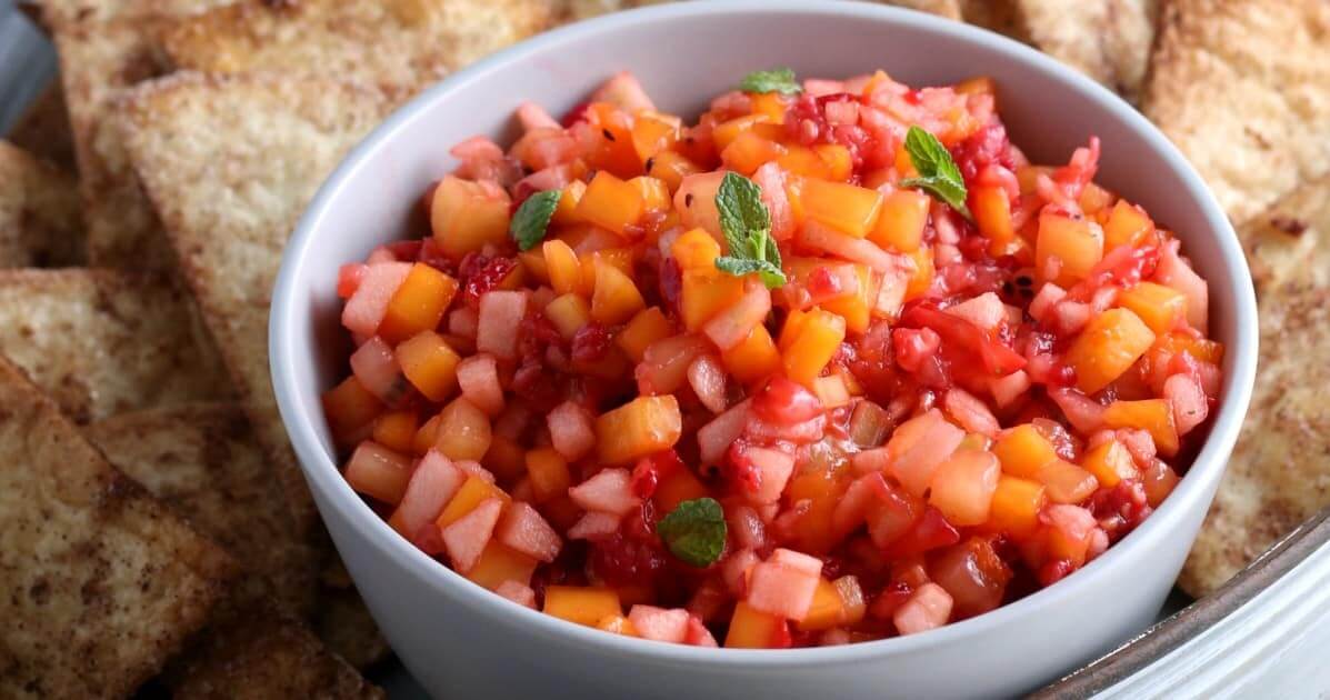 Wide photo of an extreme close-up of small diced fruit mixed together and in a bowl with cinnamon chips.