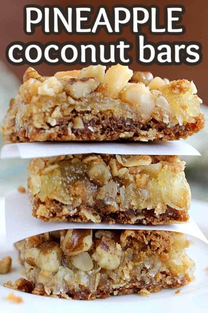 Three pineapple coconut bars stacked on top of each other with parchment squares between each golden bar.