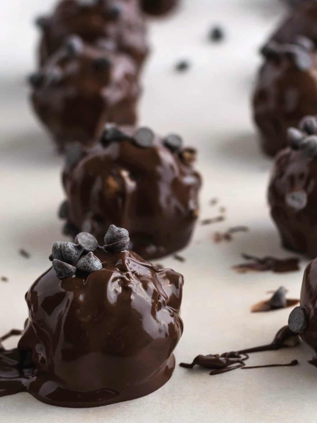 Close up view of the no bake recipe just as the chocolate covered balls are placed on parchment paper so the chocolate is glistening.