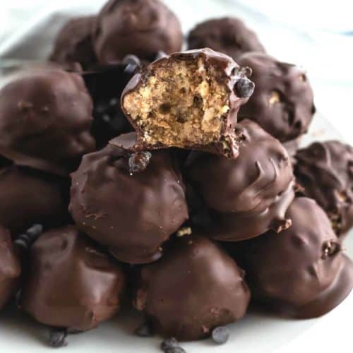 Close up photo of a pile of chocolate balls with a bite out of the top front one so show the rice Krispie treat inside.