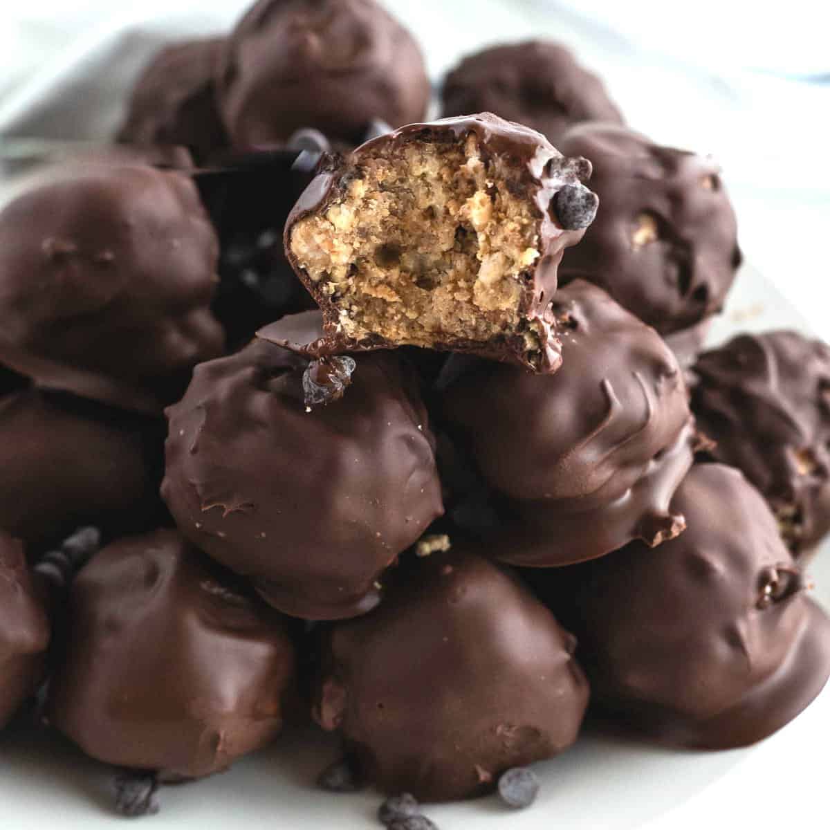 Close up photo of a pile of the chocolate balls no bake recipe with a bite out of the top front ball to show the rice Krispie treat inside.