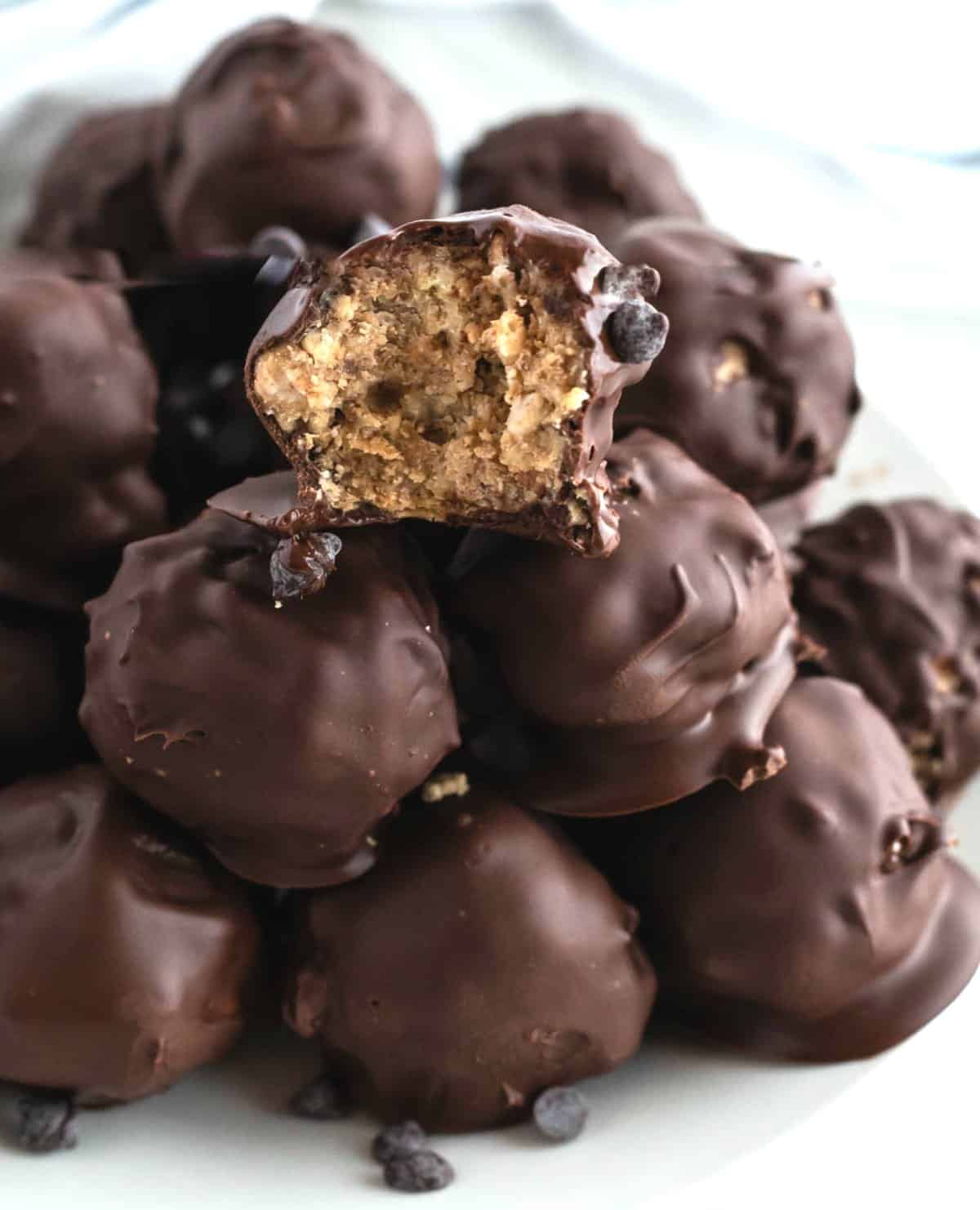 A pile of the no bake recipe showing the chocolate covered candy treats against a white background. A bite is taken out of the top ball to show the crunchy inside.