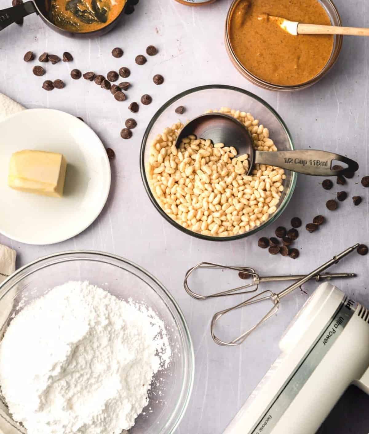 Overhead photo of ingredients for rice krispie peanut butter balls with a mixer and chocolate scattered around.