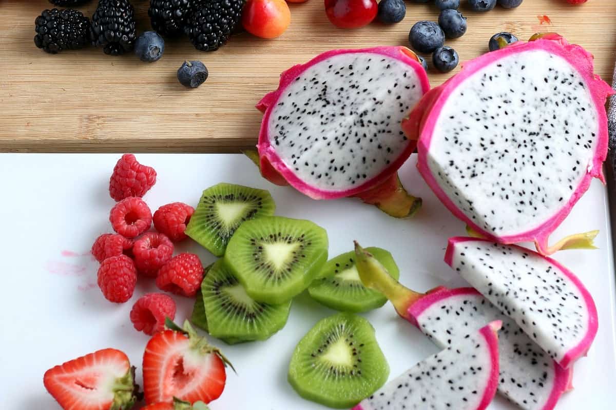 Pieces of dragon fruit, kiwi and strawberries and more are being sliced for the topping.