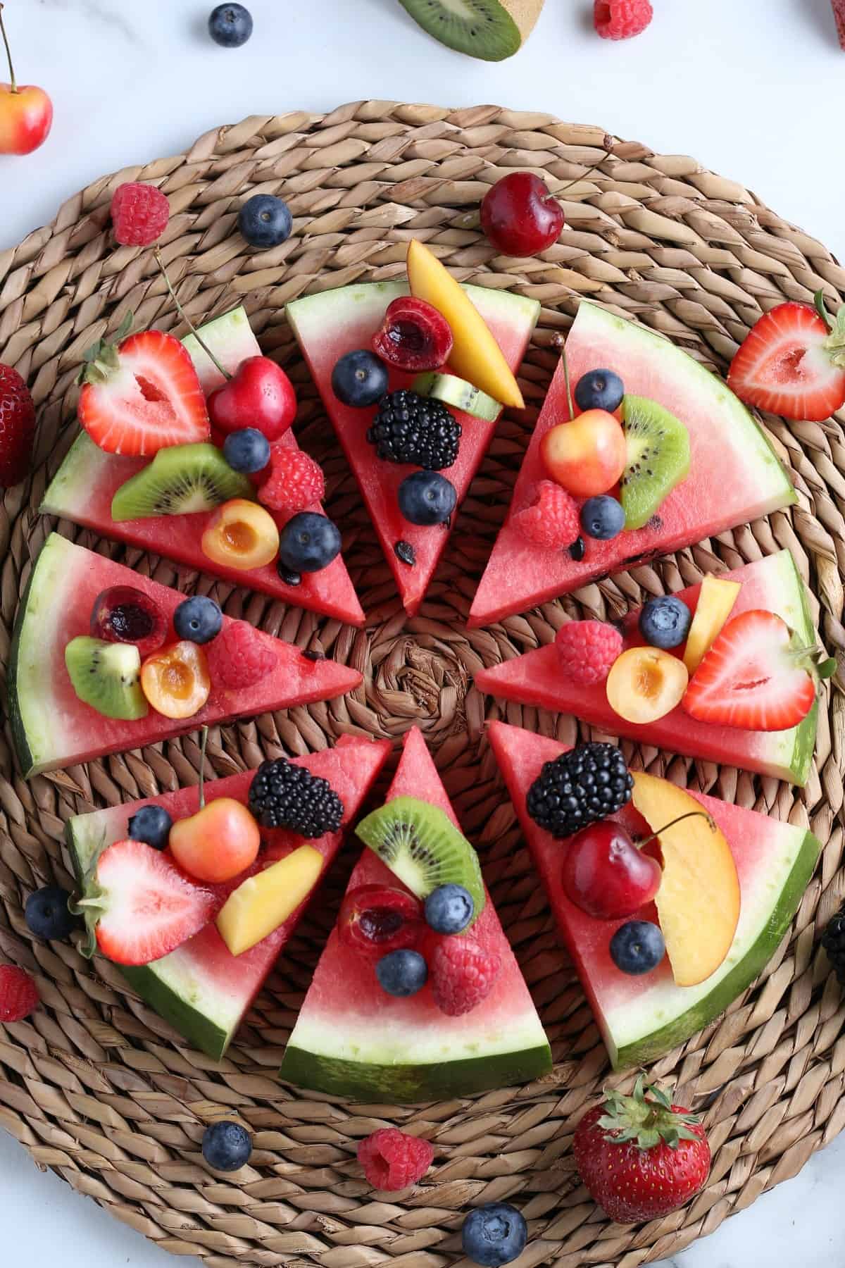 Overhead of sliced red melon round covered with berries and more and then sliced into wedges for serving.