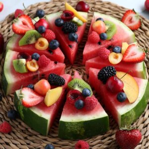 Angled thick slice of watermelon covered with fresh fruit pieces and then sliced into wedges for serving.