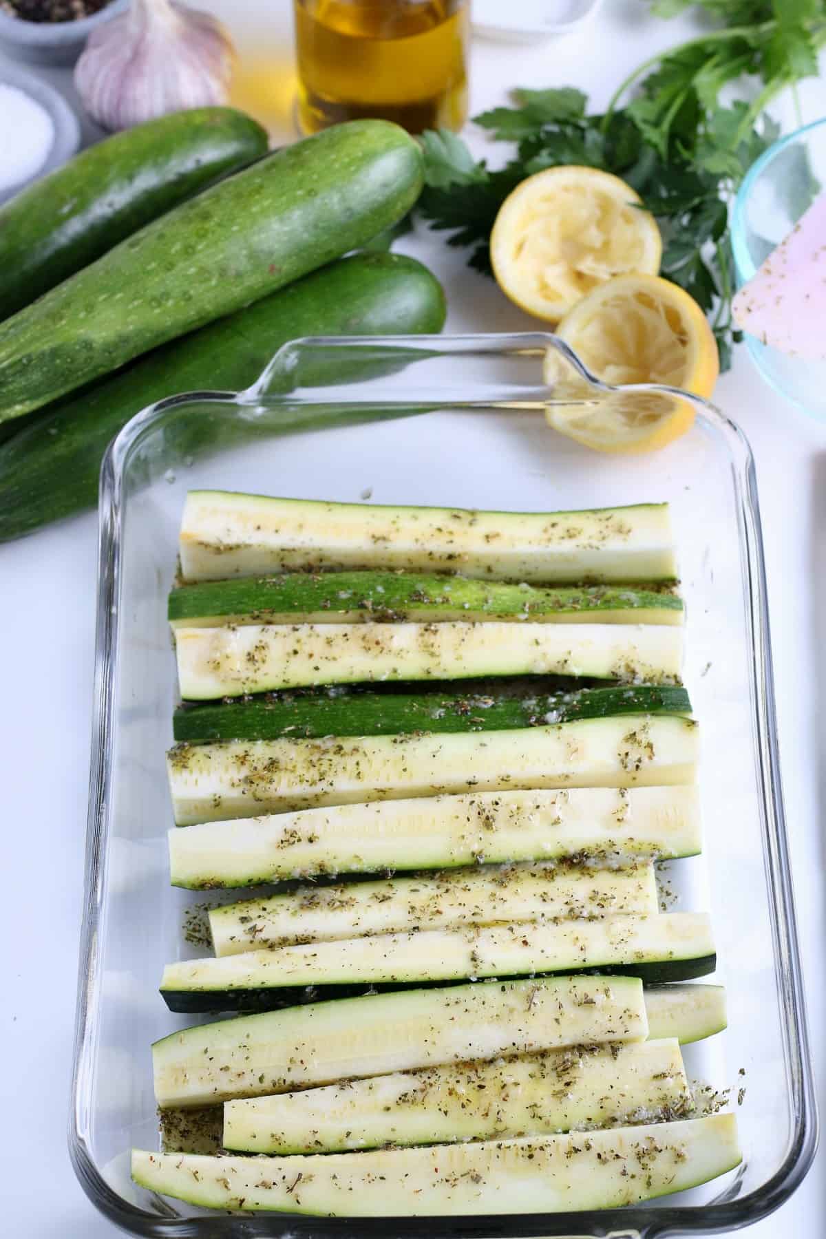 Slice zucchini are laid out on a long casserole with the herbed marinade brushed all over the top.
