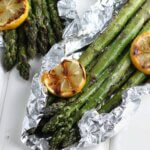 Close up photo of two open foil packets filled with grilled asparagus and grilled lemon slices.