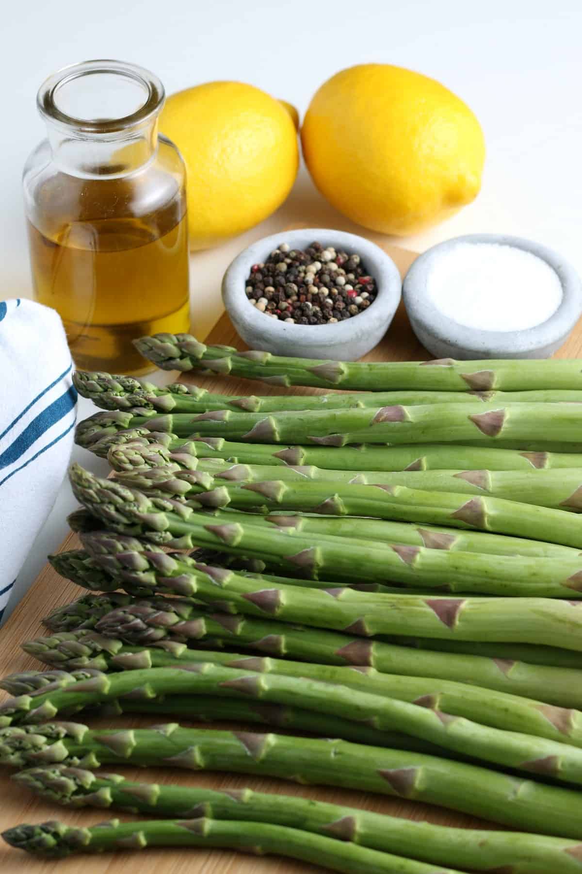 Fresh asparagus is laying side by side on a cutting board along with ingredients necessary for grilling.