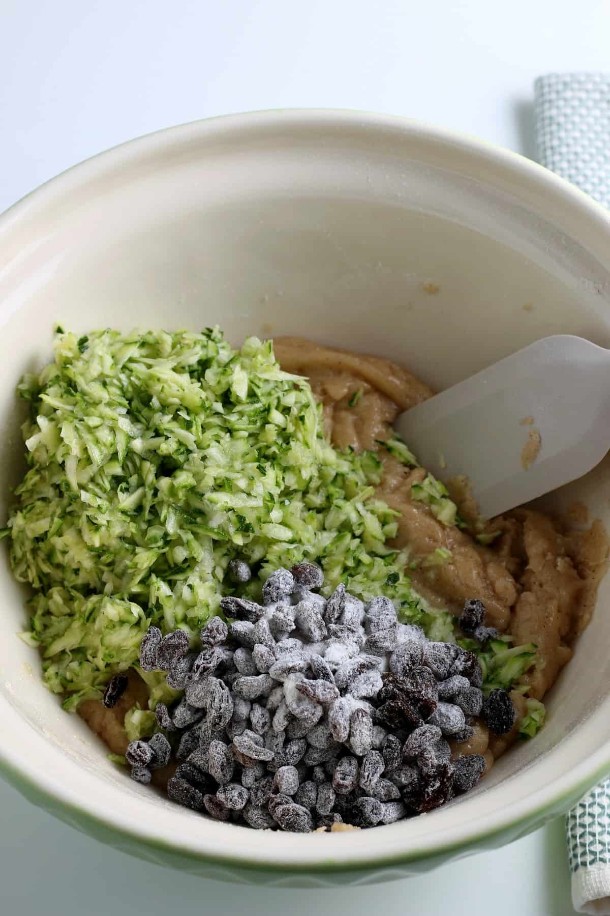 Overhead view of muffin batter with grated zucchini and coated raisins waiting to be combined.