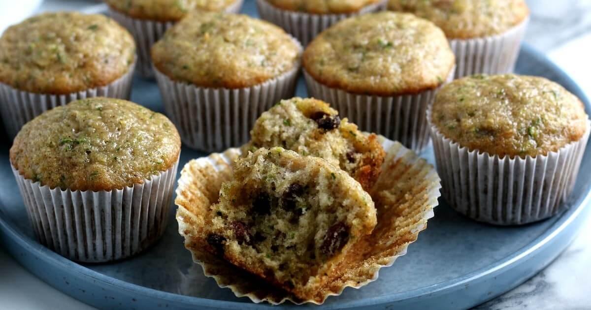 A wide angled view of a tray of muffins with one broken open so you can see the mpist inside with zucchini and raisins.
