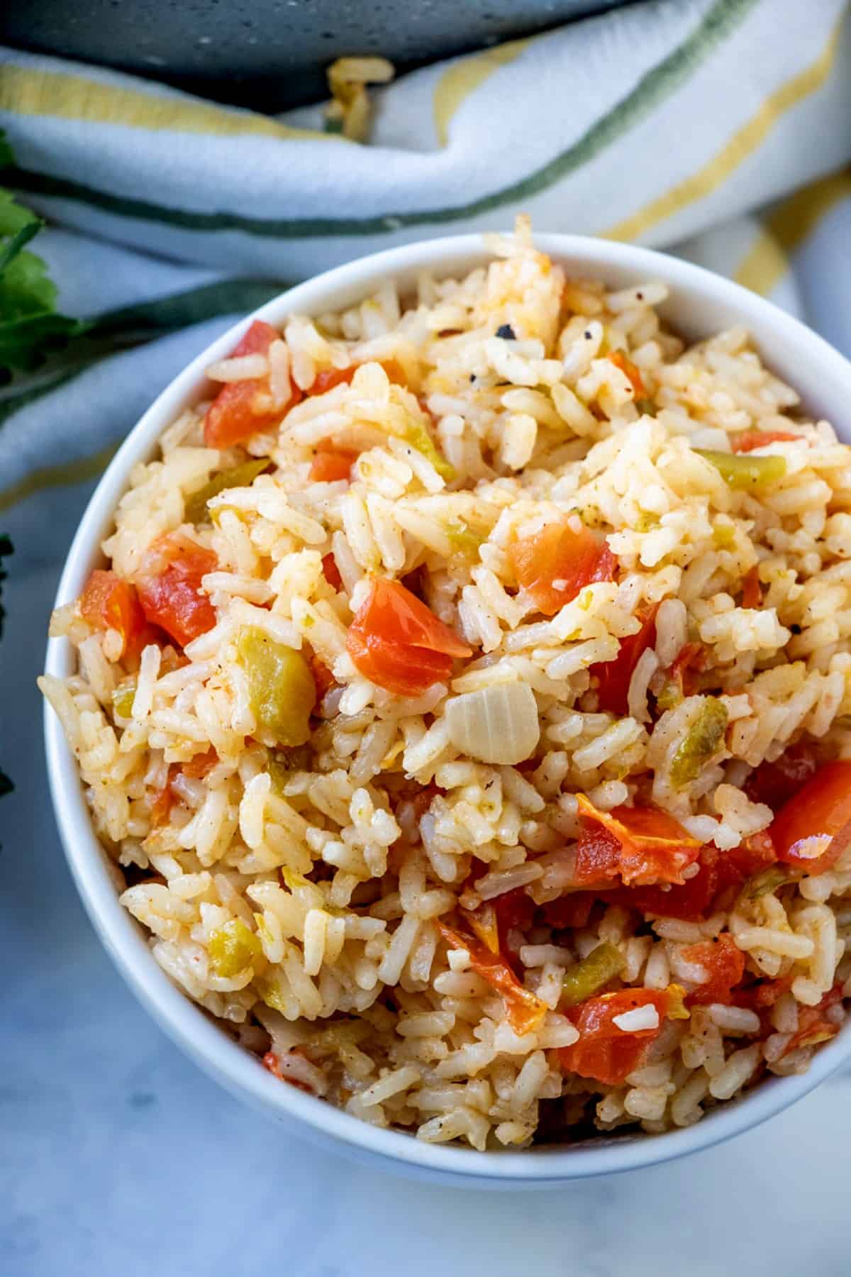 Spanish rice is in an overhead view and is showing off the canned green chilies and tomato pieces. A striped hand towel is on the side.