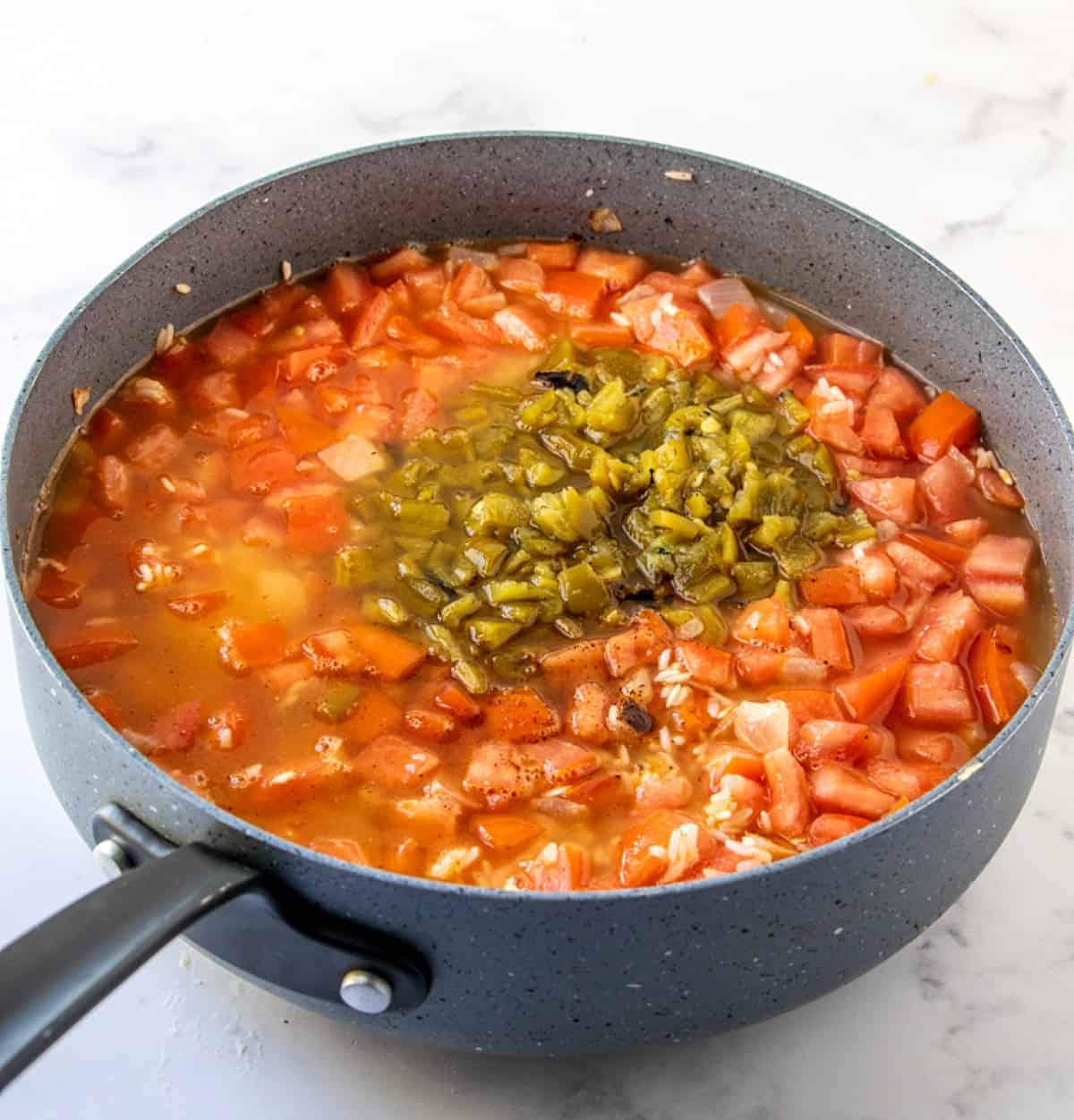 A skillet fu/l of all of the ingredients to cook down to a tasty Spanish rice with green chilies on top.