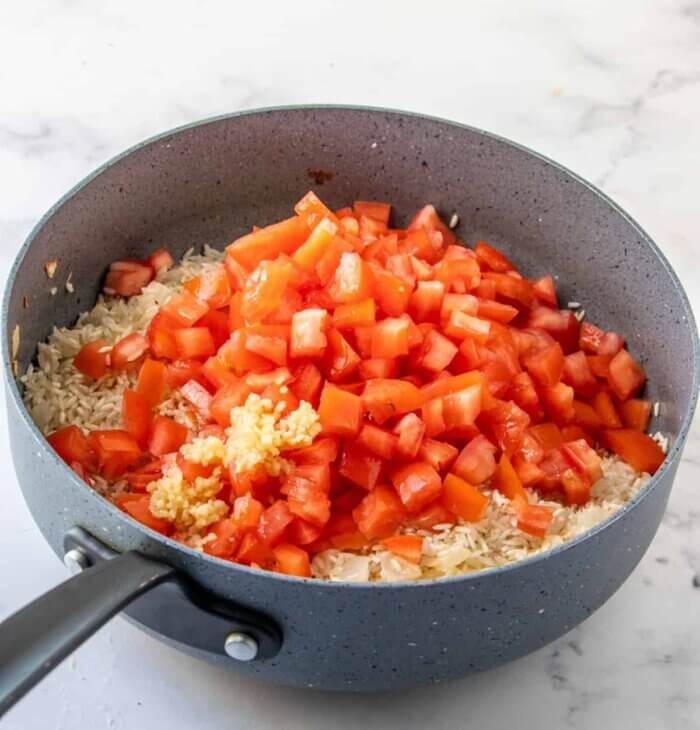 A skillet is holding fresh chopped tomatoes on the sautéd onions, garlic, and rice.