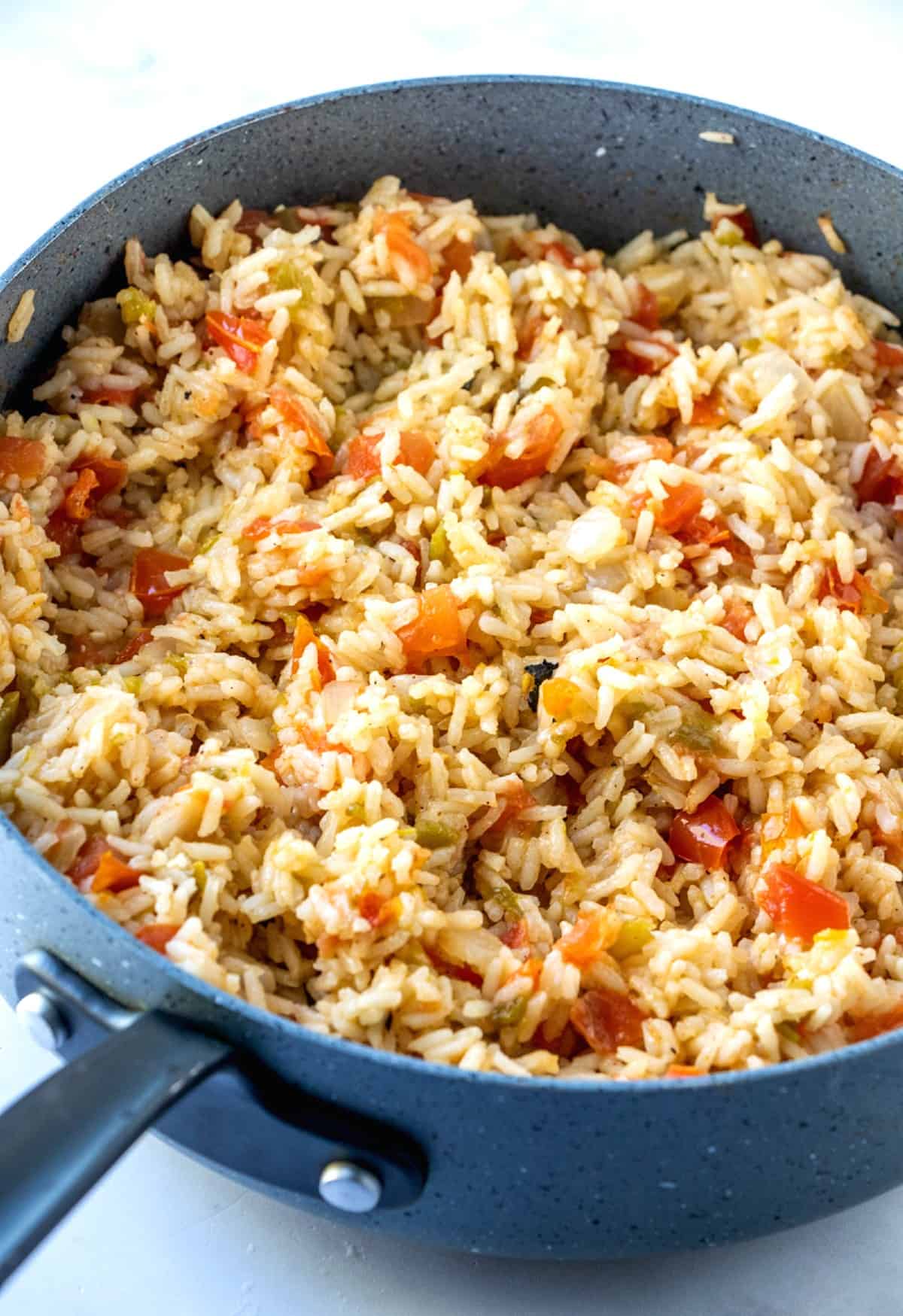 Close-up photo of rice, tomatoes and green chilies in the pan after all of the extra liquid has been cooked away and the rice is fluffed.