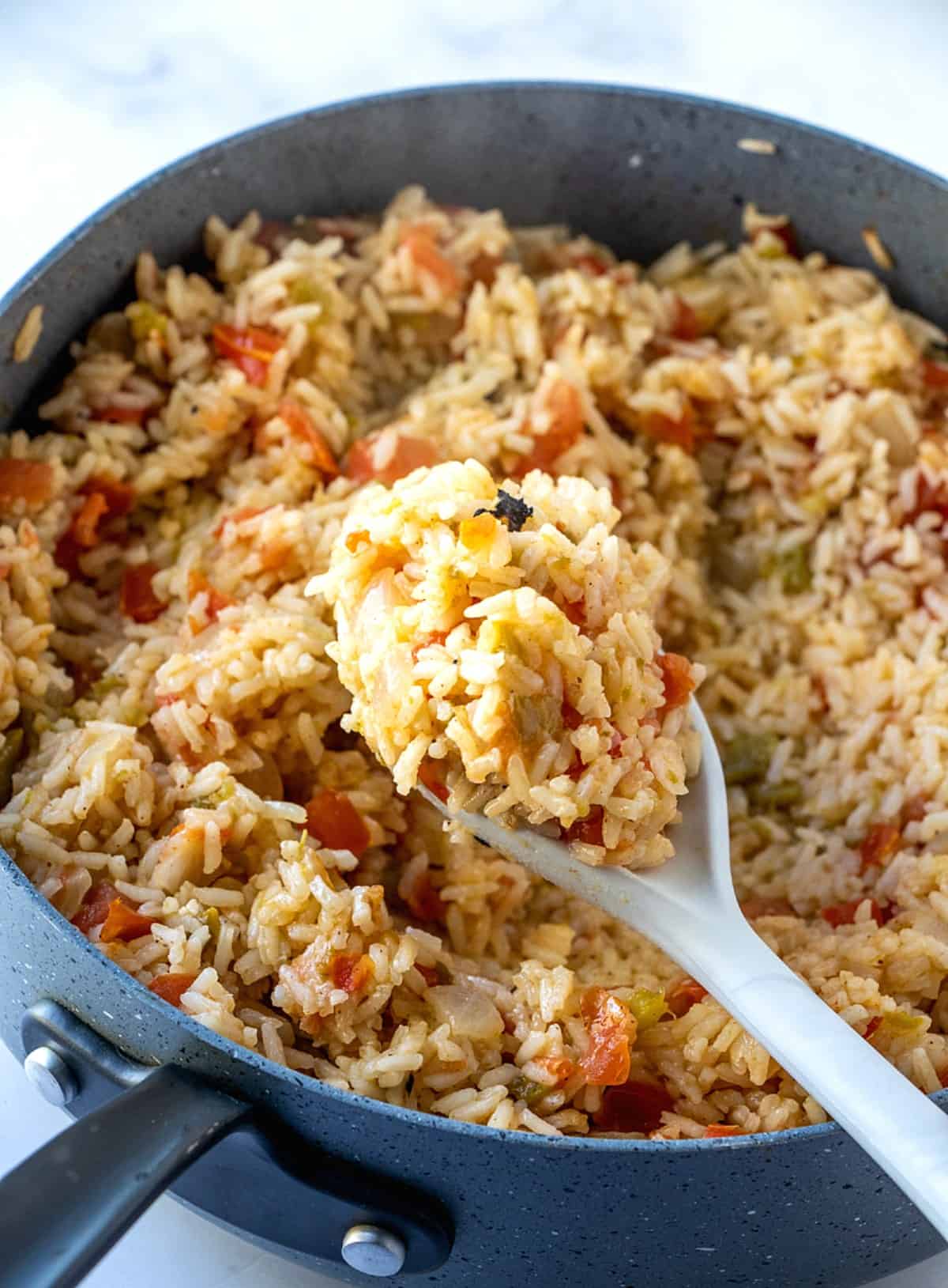 A wooden spoon has scooped up a mound of Spanish rice close to the lens so that we can see all of the ingredients inside.