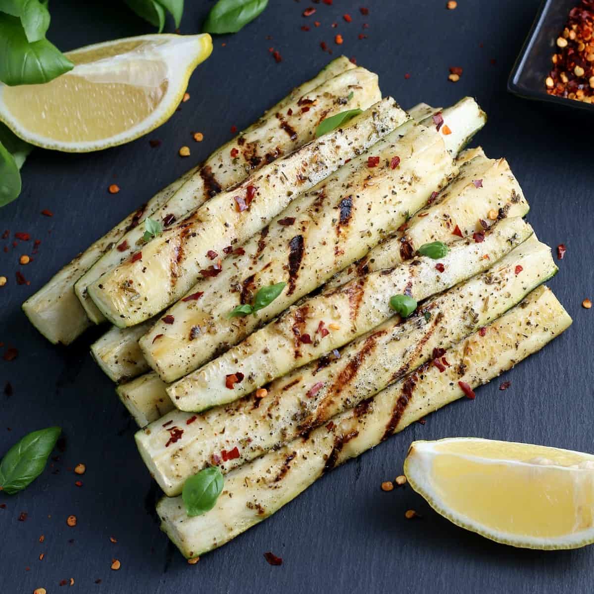 Overhead photo of grilled zucchini spears stacked in a pyramid with lemon wedges on the side.