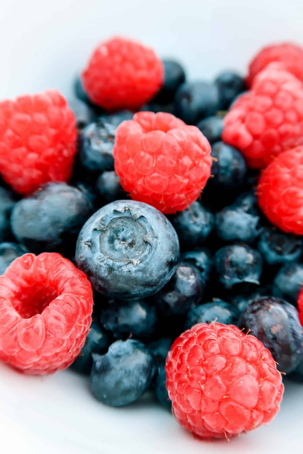 A stack of fresh blueberries and raspberries against white waiting to be added to your alcoholic beverages.
