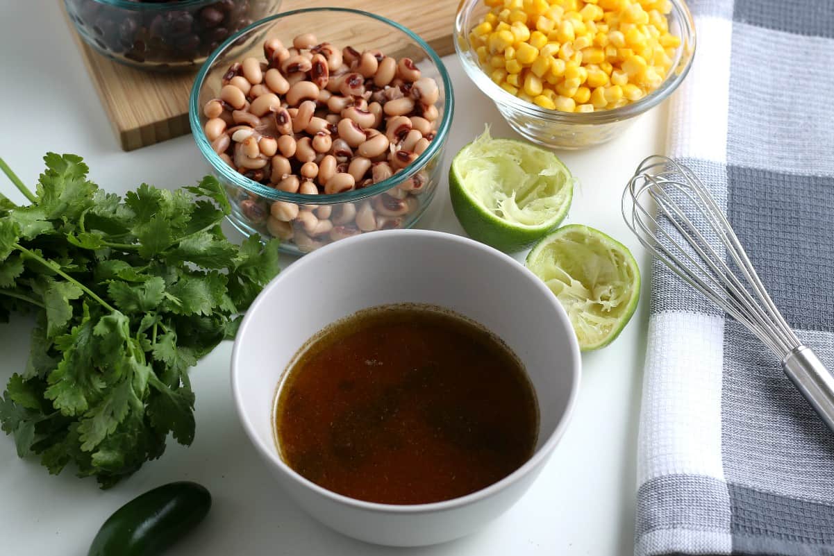 The mixed dressing is in a white bowl sitting in front of corn, black eyes peas and squeezed lime.