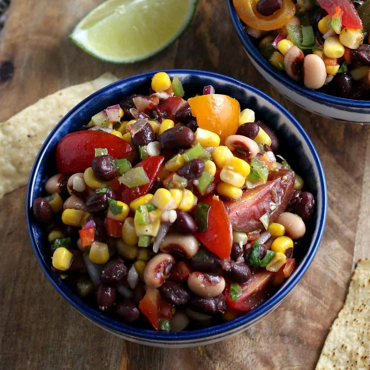 Overhead view of cowboy caviar in a blue bowl showing corn, beans and more veggies all waiting to be dipped with a chip.