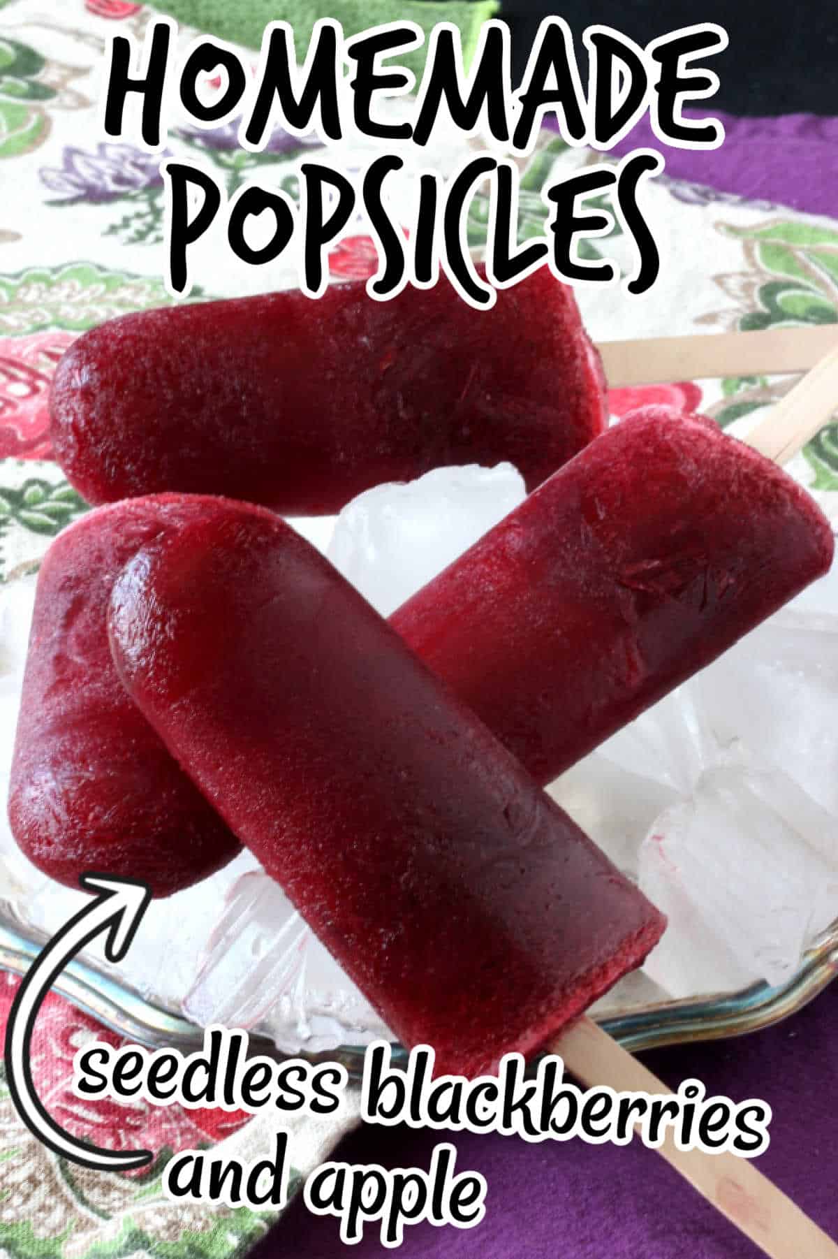 Four deep blackberry colored popsicles laying criss-cross on top of each other and on a bed of ice in a tray. Text overlay for pinning.