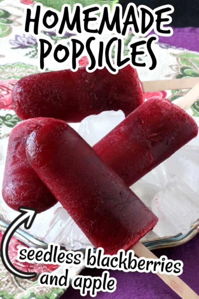 Four seedless blackberry popsicles laying criss-cross on top of each other and on a bed of ice in a silverplate tray with text overlay for pinning.