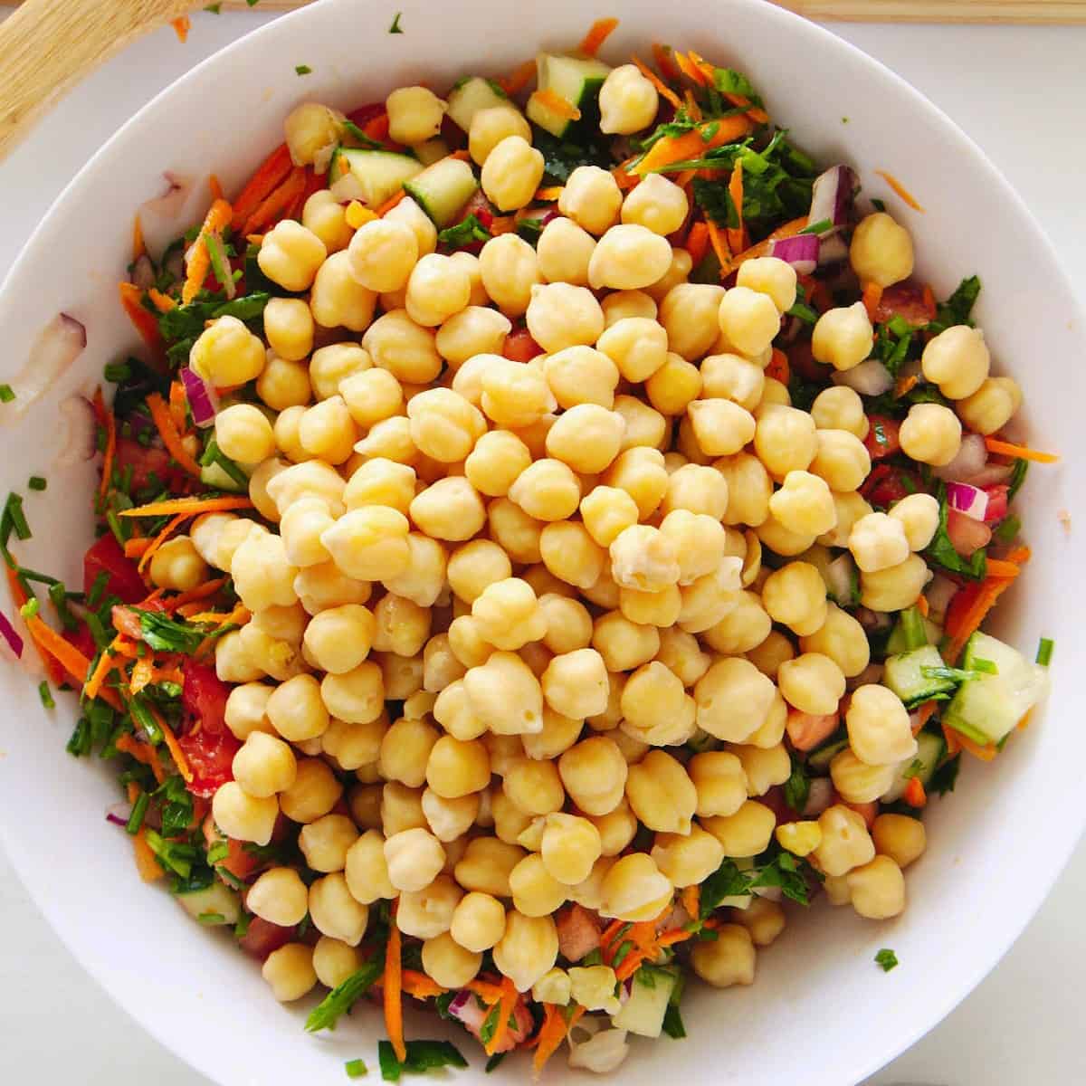 The final vegetable, canned chickpeas, is added to the salad mixture in this overhead view.