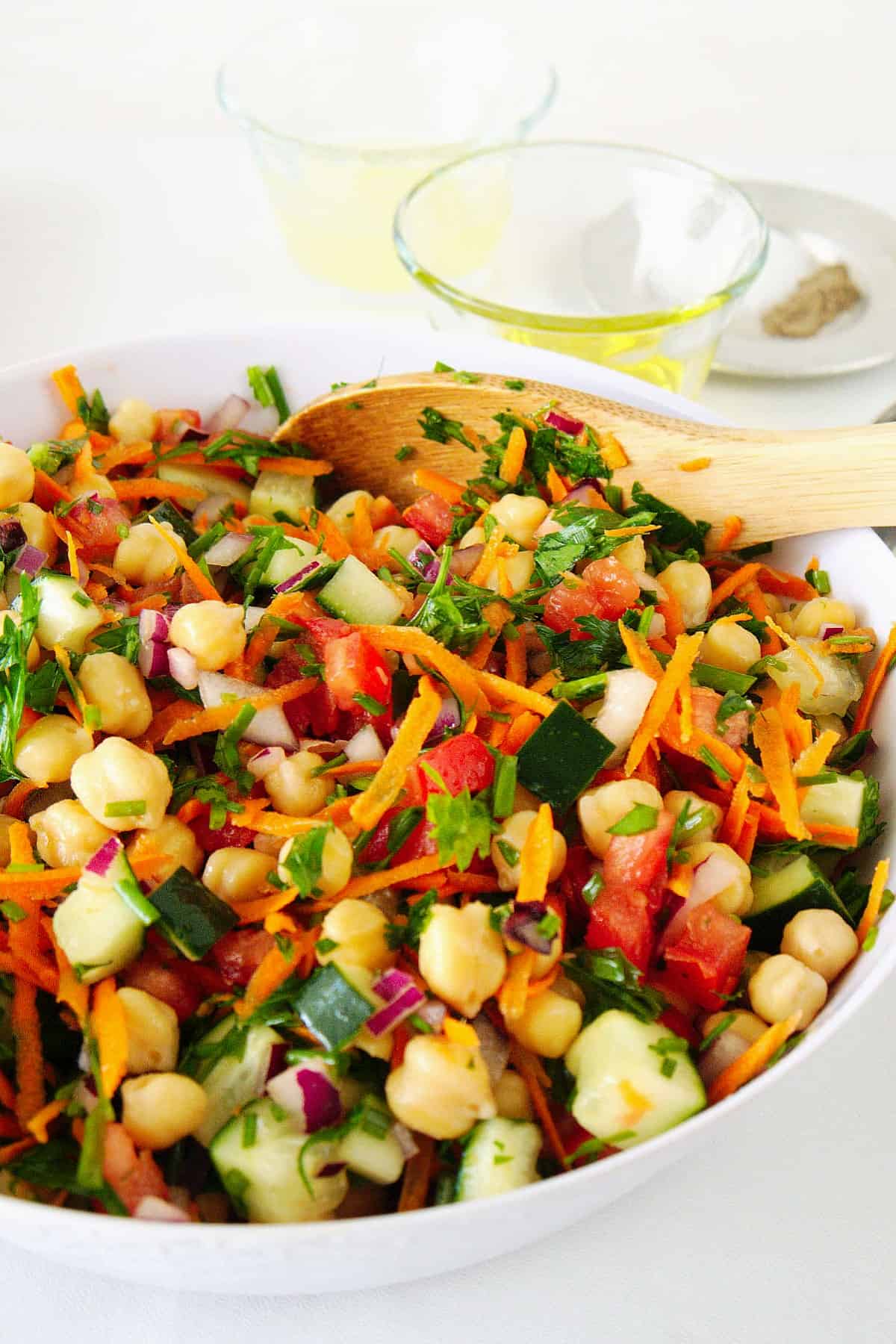 Angled bowl of healthy veggies mixed in a white bowl with a wooden spoon stuck in the side.