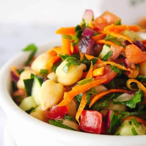 Close up sideways view of colorful Mediterranean Chickpea salad in a white bowl against a white background.