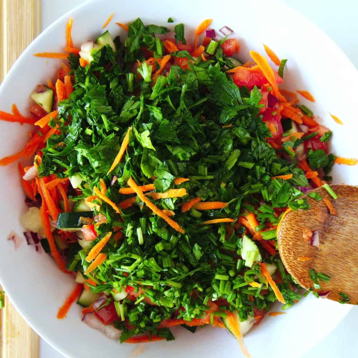 Cucumber, shredded carrot and fresh chopped parsley is added to the tomatoes and onions in an overhead shot.