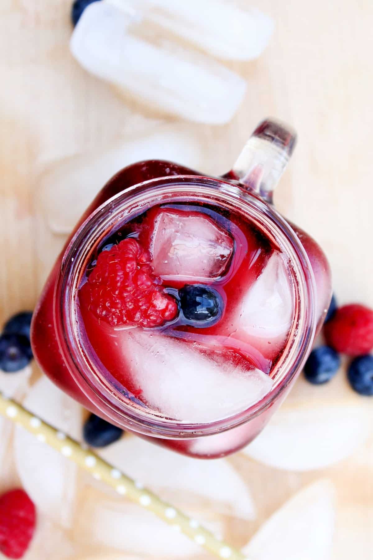 Overhead view looking down into a glass mug with red wine and berries over ice. Ice cubes are around the glass too.