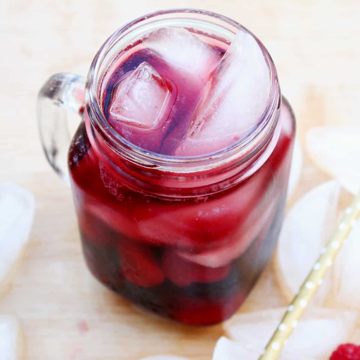 A glass mug with the handle on the left and red wine sangria is filling the glass with alcoholic beverages and berries.