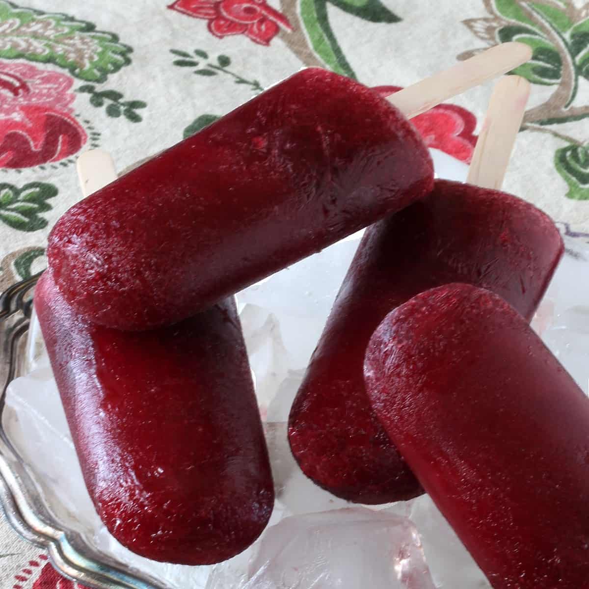 Four seedless blackberry popsicles laying criss-cross on top of each other and on a bed of ice in a silverplate tray.